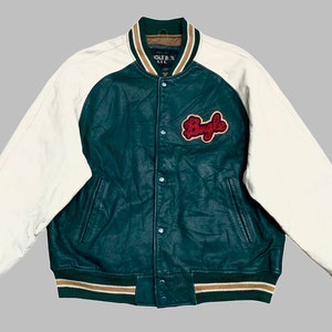 May include: A green leather varsity jacket with white sleeves and a brown and green striped collar. The jacket has a large "Bugle" patch on the right side of the chest.