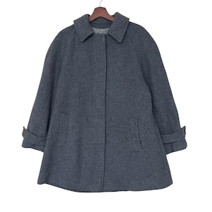 May include: A grey wool coat with a rounded collar and two front pockets. The coat has long sleeves with buttoned cuffs and a button closure down the front. The coat is hanging on a wooden hanger against a white background.
