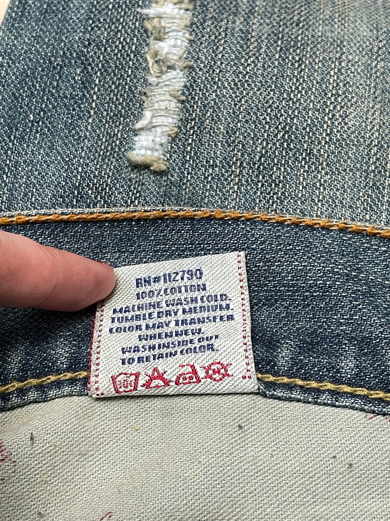 May include: A white care label with black text that reads "RN#112790 100% COTTON MACHINE WASH COLD TUMBLE DRY MEDIUM COLOR MAY TRANSFER WHEN NEW. WASH INSIDE OUT TO RETAIN COLOR."