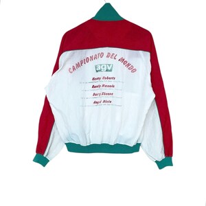 May include: Red, white, and green vintage jacket with the text "CAMPIONATO DEL MONDO" and the "agv" logo. The back of the jacket features the names of Kenny Roberts, Randy Mamola, Barry Sheene, and Angel Nieto.