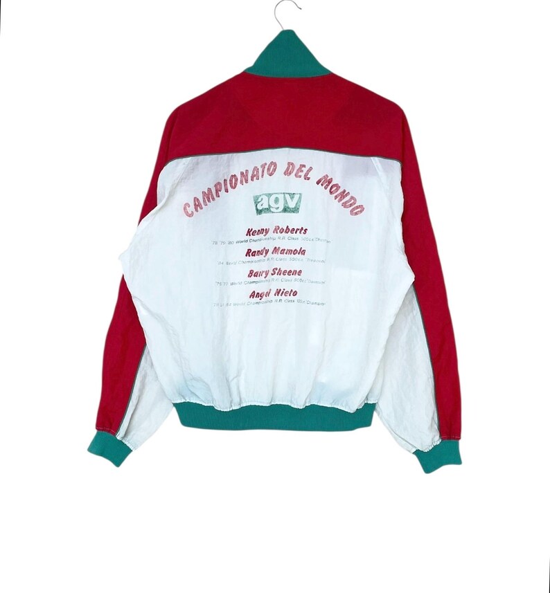 May include: Red, white, and green vintage jacket with the text "CAMPIONATO DEL MONDO" and the "agv" logo. The back of the jacket features the names of Kenny Roberts, Randy Mamola, Barry Sheene, and Angel Nieto.