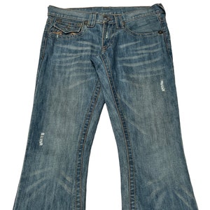 May include: A pair of blue denim jeans with a bootcut leg style. The jeans have a distressed look with several small holes and faded areas. The jeans have a light wash and a classic five-pocket style.