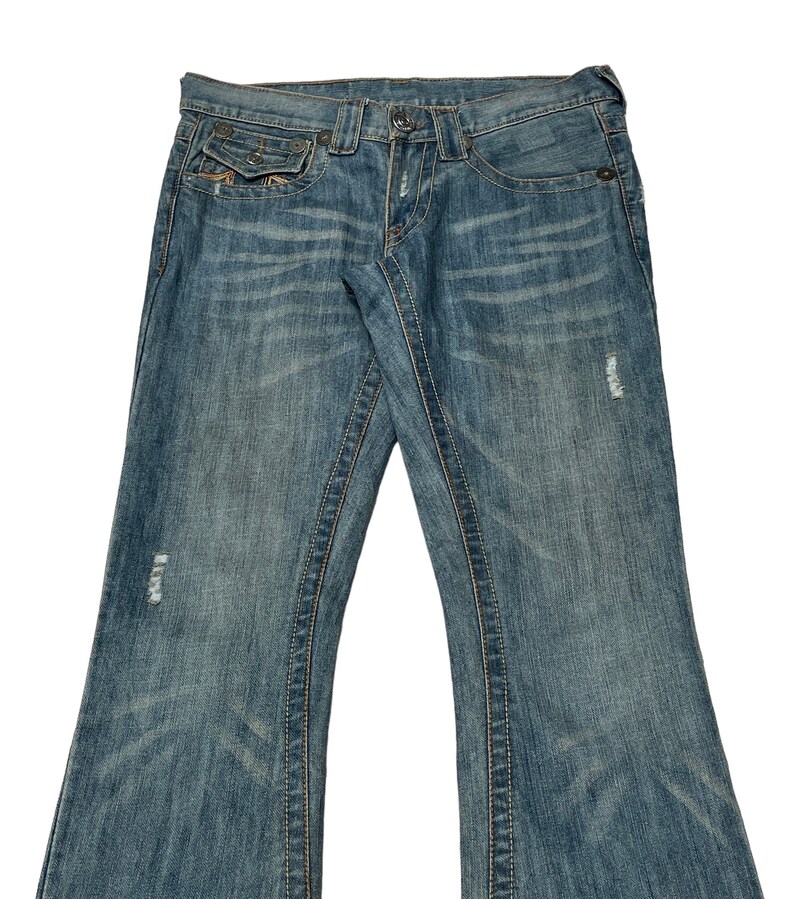 May include: A pair of blue denim jeans with a bootcut leg style. The jeans have a distressed look with several small holes and faded areas. The jeans have a light wash and a classic five-pocket style.