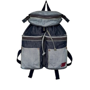 May include: A blue denim backpack with multiple pockets and a drawstring closure. The backpack has a brown leather accent on the top flap.