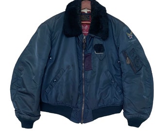 May include: A dark blue bomber jacket with a black faux fur collar and a zipper closure. The jacket has a patch on the left sleeve that says "U.S. AIR FORCE".