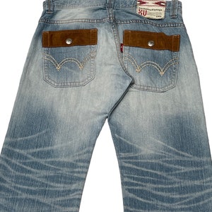 May include: Light blue denim jeans with brown suede patch pockets and stitching detail. The back pockets have a red and white label with the text "Exclusive Vintage RU" and "2014".