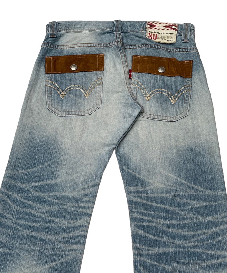 May include: Light blue denim jeans with brown suede patch pockets and stitching detail. The back pockets have a red and white label with the text "Exclusive Vintage RU" and "2014".