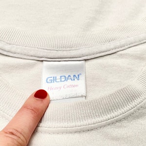 Op de afbeelding: Wit Gildan T-shirt met een wit label met de tekst "Gildan Heavy Cotton".