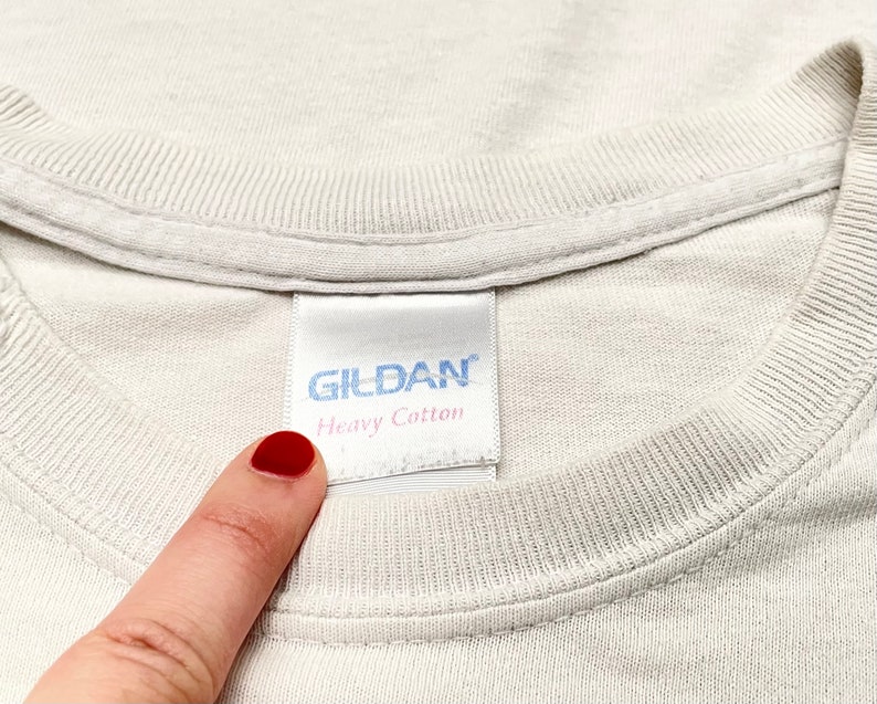 Op de afbeelding: Wit Gildan T-shirt met een wit label met de tekst "Gildan Heavy Cotton".