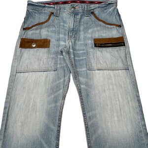 May include: Light blue denim jeans with brown suede patches and a zippered pocket. The jeans have a straight leg and a relaxed fit.