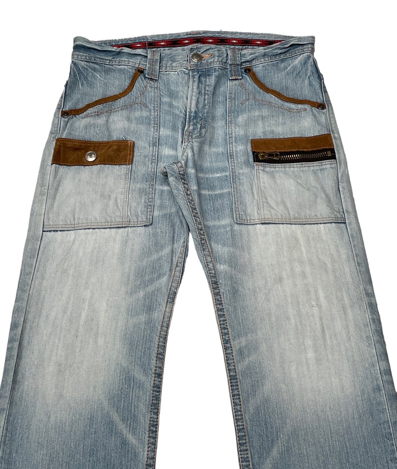 May include: Light blue denim jeans with brown suede patches and a zippered pocket. The jeans have a straight leg and a relaxed fit.