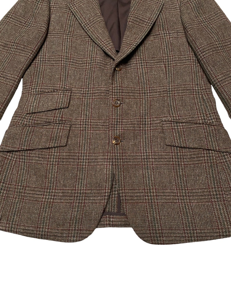 K&ouml;nnte beinhalten: Ein brauner Tweed-Blazer mit Karomuster. Der Blazer hat einen Schalkragen, einen Zwei-Knopf-Verschluss und zwei Pattentaschen.