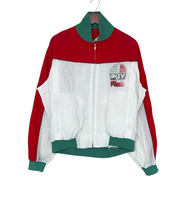 May include: A vintage red, white, and green zip-up jacket. The jacket features red sleeves and upper back, a white front, and green accents on the collar, cuffs, and hem. The chest has a small logo that reads "agv".