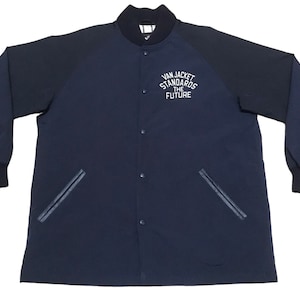 Pode incluir: Uma jaqueta bomber azul marinho com um logotipo branco bordado que diz "Van Jacket Standards The Future". A jaqueta tem dois bolsos e uma gola canelada.