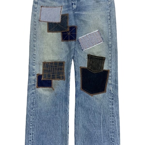 May include: Light blue denim jeans featuring a patchwork design with various blue and white fabrics. Patches include striped and patterned textiles, giving a handcrafted look. The jeans have a classic five-pocket design.