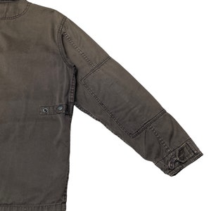 Puede incluir: Una chaqueta de trabajo marr&oacute;n oscuro con cierre de botones y un bolsillo con solapa en la manga izquierda.