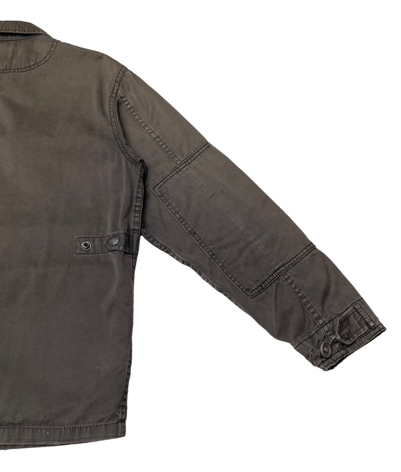 Puede incluir: Una chaqueta de trabajo marr&oacute;n oscuro con cierre de botones y un bolsillo con solapa en la manga izquierda.