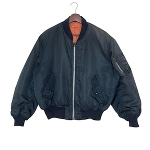 May include: A dark blue bomber jacket with a zipper closure and a contrasting orange lining. The jacket has a pocket on the left sleeve and a ribbed knit collar, cuffs, and waistband.