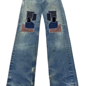 May include: Blue denim jeans with multiple patches of different coloured fabrics sewn on the front of the legs.