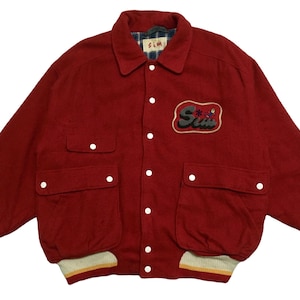 May include: A red wool varsity jacket with a large embroidered patch that says "Sum" in a retro font. The jacket has a button-up front, two large pockets, and ribbed cuffs and hem.
