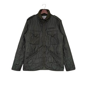 May include: A dark green quilted jacket with a zipper closure and a stand-up collar. The jacket has two large flap pockets on the front and a smaller pocket on the left chest. The word "AVIREX" is embroidered on the right chest pocket.