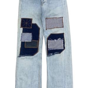 May include: Light blue denim jeans with multiple patches of different colored fabrics sewn on the front of the legs.