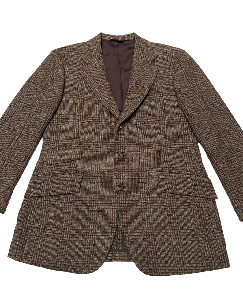 K&ouml;nnte beinhalten: Ein brauner Blazer mit Karomuster und einem Knopfverschluss. Der Blazer hat zwei Pattentaschen auf der Vorderseite und ein braunes Futter.