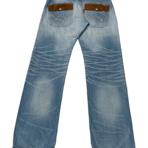 May include: A pair of light blue denim jeans with brown suede patch pockets on the back. The jeans have a distressed look and are faded in places.