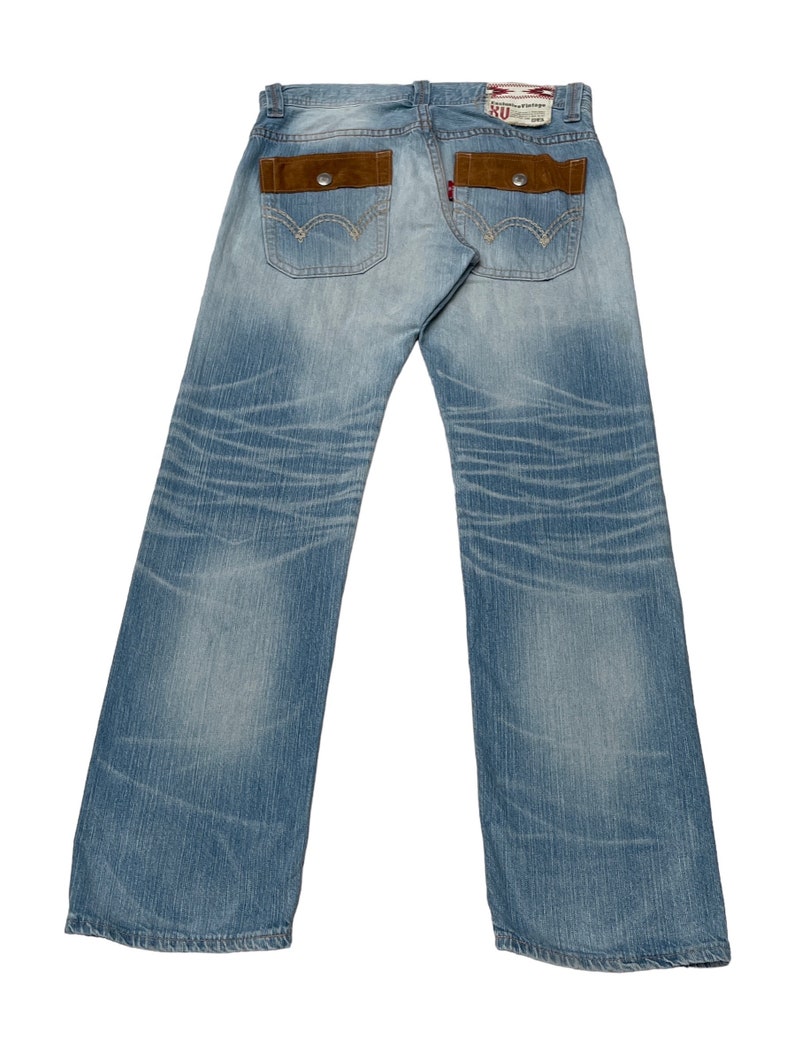 May include: A pair of light blue denim jeans with brown suede patch pockets on the back. The jeans have a distressed look and are faded in places.