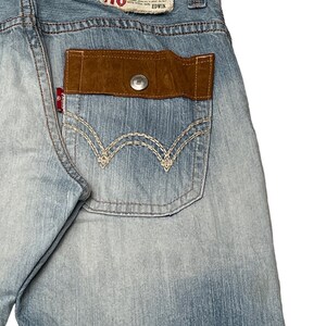 May include: Light blue denim jeans with a brown suede patch on the back pocket. The patch has a button and the words "Exclusive Vintage" and "EDWIN" are printed on a red label above the patch.