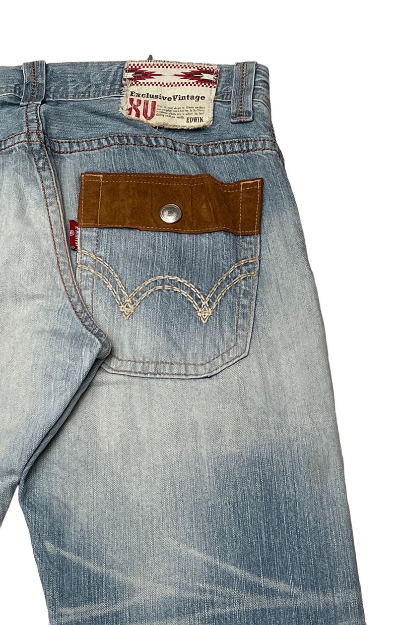 May include: Light blue denim jeans with a brown suede patch on the back pocket. The patch has a button and the words "Exclusive Vintage" and "EDWIN" are printed on a red label above the patch.