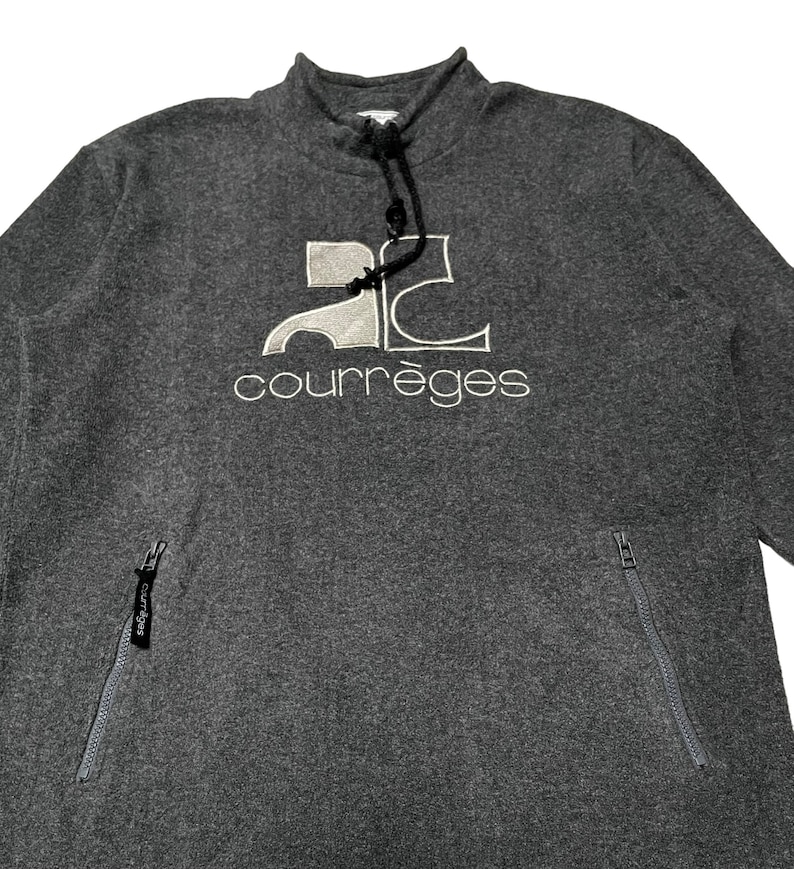 May include: Gray sweatshirt with a white embroidered logo that says "Courr&egrave;ges" and a white embroidered logo of the letter "C" with a stylized "2" inside. The sweatshirt has two zippered pockets on the sides.
