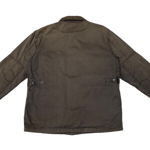 Puede incluir: Una chaqueta de trabajo marr&oacute;n oscuro con cierre de botones y dos bolsillos de solapa en el pecho. La chaqueta tiene un corte holgado y est&aacute; hecha de un tejido de algod&oacute;n resistente.