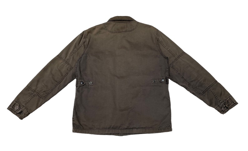 Puede incluir: Una chaqueta de trabajo marr&oacute;n oscuro con cierre de botones y dos bolsillos de solapa en el pecho. La chaqueta tiene un corte holgado y est&aacute; hecha de un tejido de algod&oacute;n resistente.