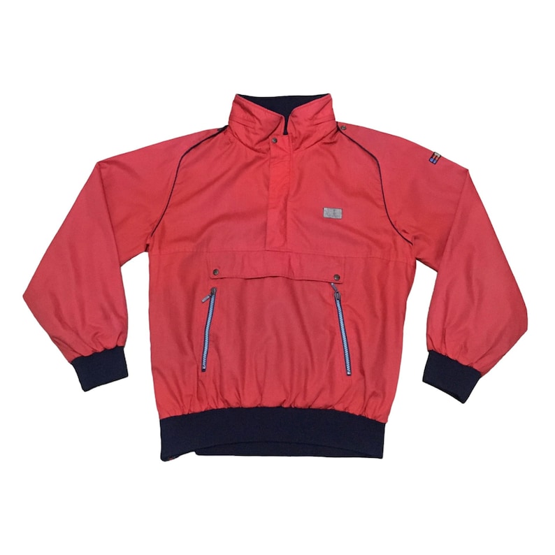 May include: A red windbreaker jacket with a high collar, zipper closure, and two zippered pockets. The jacket has a navy blue trim around the collar, cuffs, and waistband.