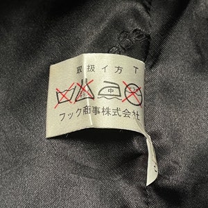 May include: A white care label with black text and symbols. The text reads "取扱イ方" and "フク商事株式会社". The symbols are for washing, ironing, and dry cleaning.