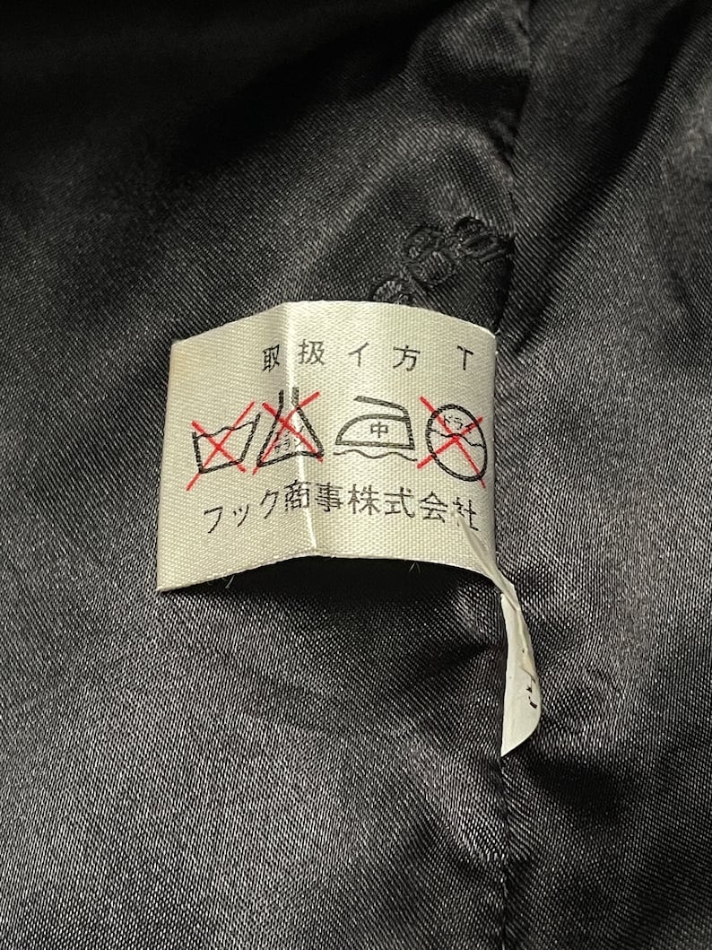 May include: A white care label with black text and symbols. The text reads "取扱イ方" and "フク商事株式会社". The symbols are for washing, ironing, and dry cleaning.