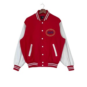Könnte beinhalten: Rote und weiße Baseballjacke mit einem weißen gestickten Logo, auf dem "Just Be Happy" und "Since 1918" in einem Kreis stehen.