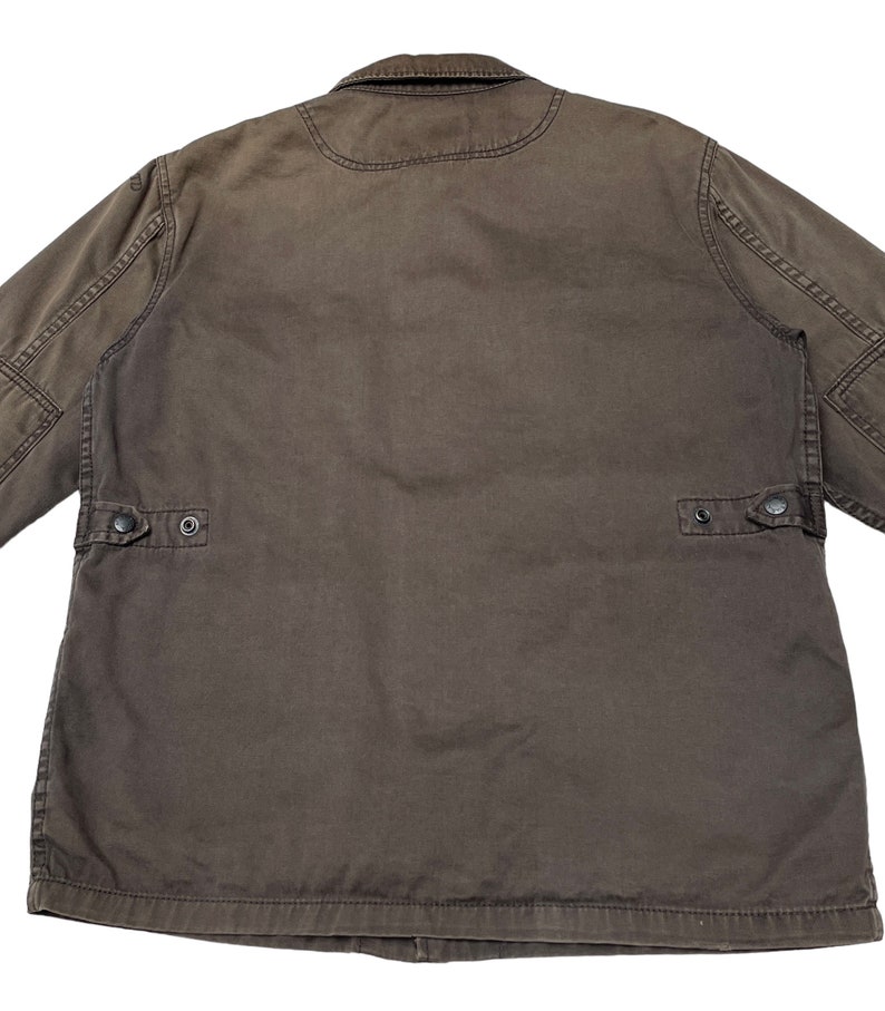 Puede incluir: Una chaqueta de trabajo marr&oacute;n con cierre de botones y dos bolsillos de solapa en la espalda.