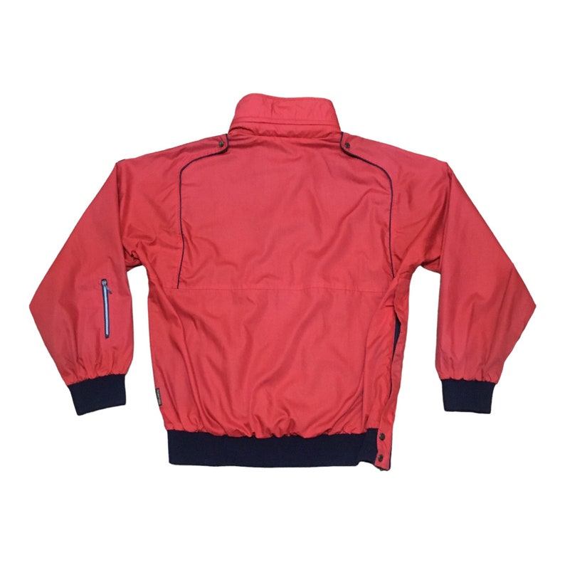 May include: A red windbreaker jacket with a navy blue zipper and trim. The jacket has a stand-up collar and a zippered pocket on the left sleeve.