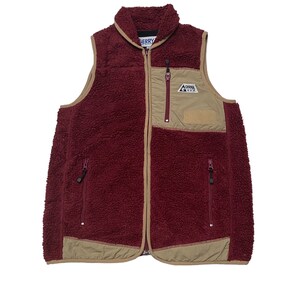 May include: A burgundy fleece vest with a zip closure and two zipped pockets. The vest has a tan coloured panel on the front with a patch that says "Gerry" in blue text.