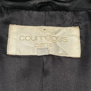 May include: A white label with the text "Courr&egrave;ges Paris" in gold lettering. The label is attached to a black leather jacket.