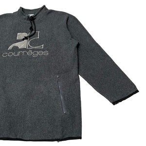 May include: Gray fleece pullover sweatshirt with a black zippered pocket on the left side. The sweatshirt has a high neck with a drawstring and features a white embroidered logo that says "2C courr&egrave;ges".