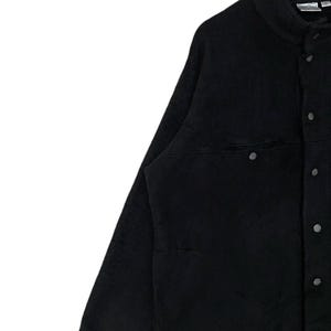 May include: A black fleece jacket with a button-up front and a single chest pocket. The jacket has a stand-up collar and long sleeves.
