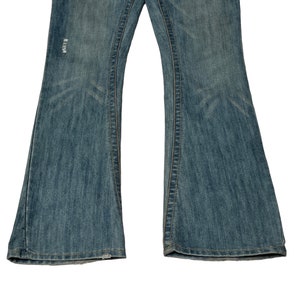 May include: A pair of blue denim jeans with a flared leg style. The jeans have a distressed look with a small hole on the left leg.