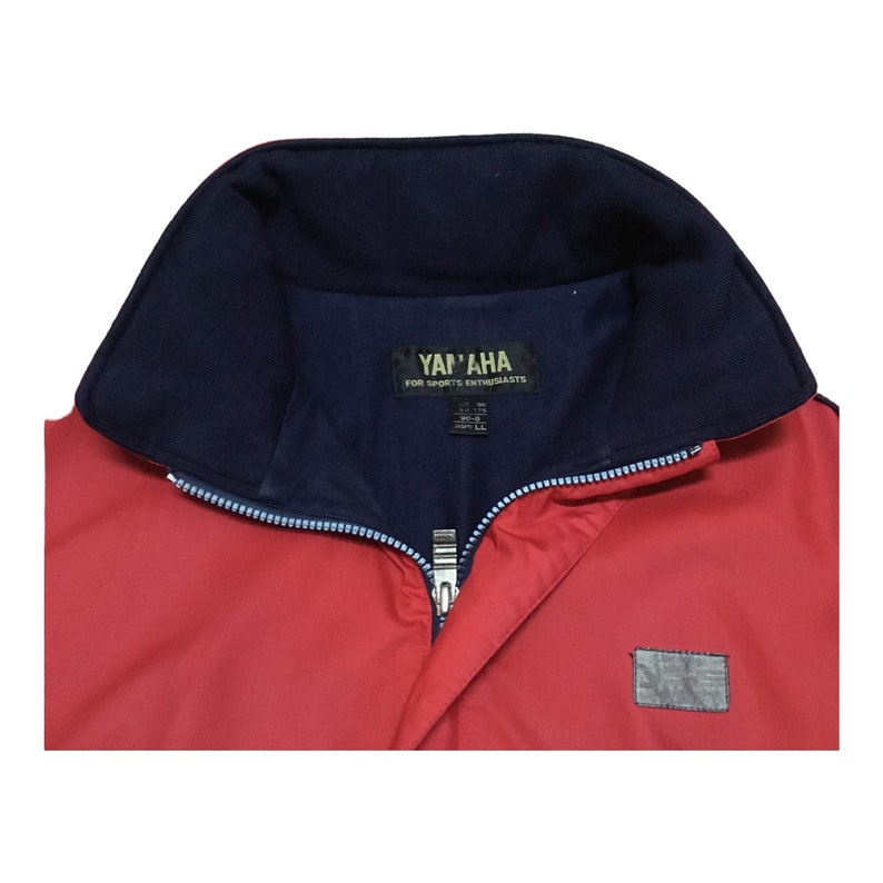 May include: Red jacket with a blue collar and a zipper closure. The jacket has a label that says "Yamaha for Sports Enthusiasts" and a small patch on the lower right side.