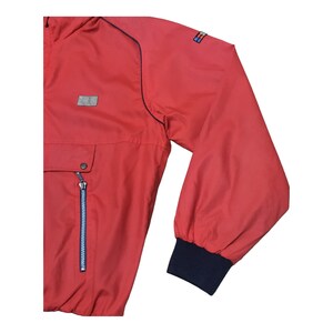 May include: Red windbreaker jacket with a blue zipper and a blue and white logo on the sleeve.