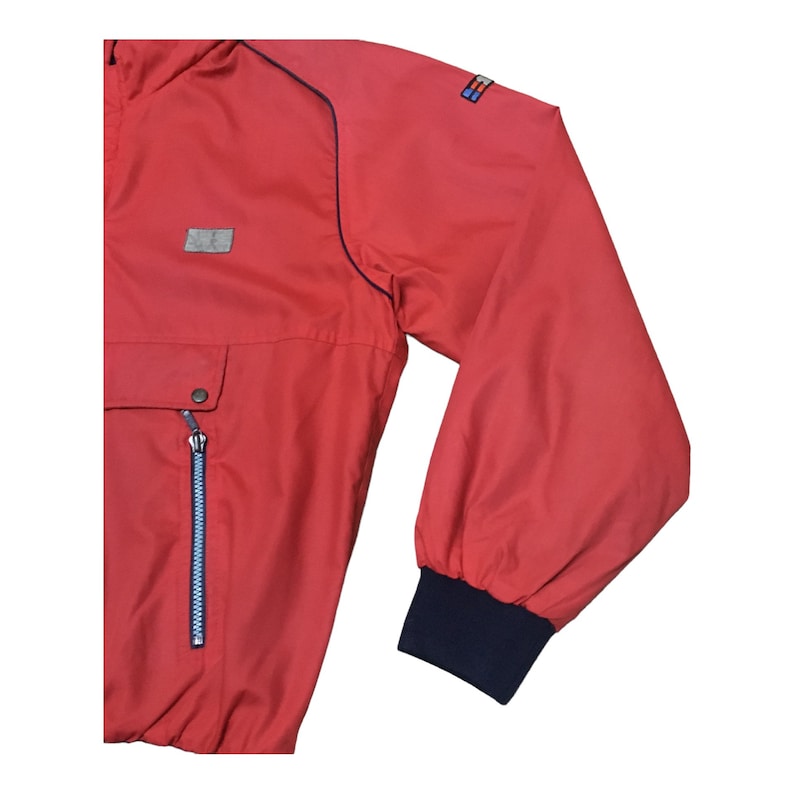 May include: Red windbreaker jacket with a blue zipper and a blue and white logo on the sleeve.