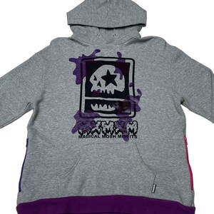 May include: Gray hooded sweatshirt with a purple skull graphic and the text "Magical Mosh Misfits". The sweatshirt has purple accents on the bottom and zipper pulls.