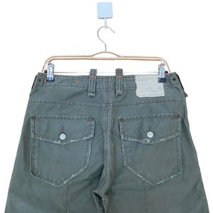 May include: A pair of green cargo trousers with two large pockets on the back. The trousers have a distressed look with frayed edges.